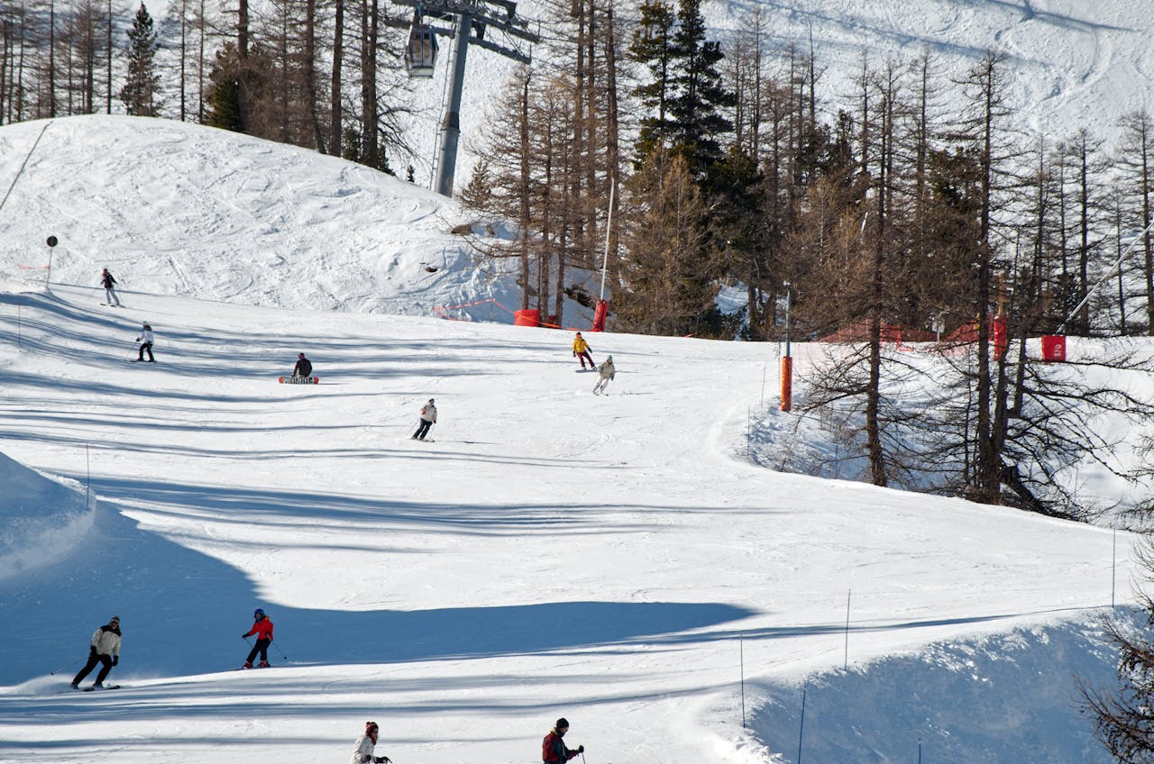 Skiers enjoying a thrilling downhill ride on a snow-covered mountain slope surrounded by bare trees.