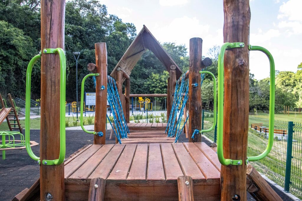 Wooden playground construction with green handrails in a Londrina park surrounded by nature.