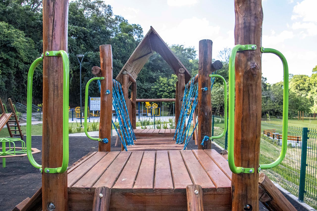 Wooden playground construction with green handrails in a Londrina park surrounded by nature.